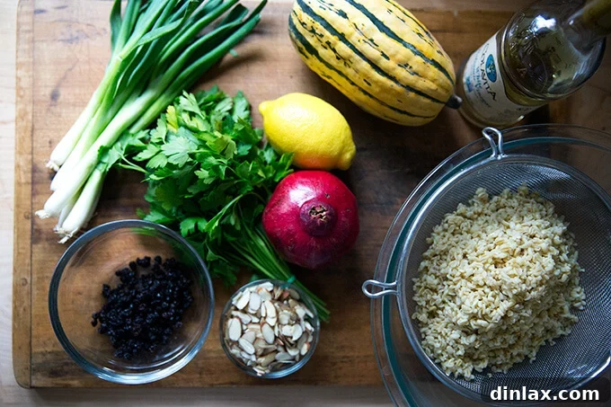 An overhead shot of a wooden cutting board laden with fresh ingredients for winter tabbouleh, including parsley, scallions, a pomegranate, soaked currants, and toasted almonds.
