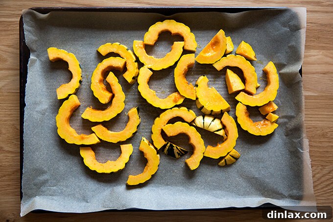 Delicata squash slices, perfectly seasoned and arranged on a parchment-lined baking sheet, prepared for roasting.