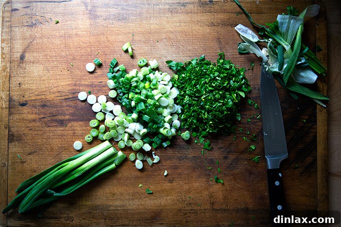 An overhead shot of a wooden cutting board showcasing freshly chopped scallions and finely minced parsley, essential herbs for tabbouleh.