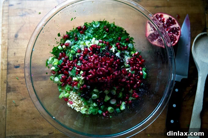 An overhead shot of a glass bowl filled with colorful winter tabbouleh, generously topped with glistening red pomegranate arils.
