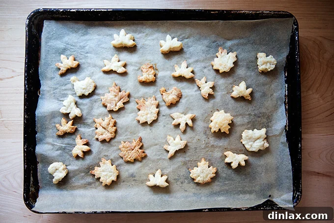 A sheet pan lined with parchment paper, topped with freshly baked, golden-brown pie cookies in various shapes.