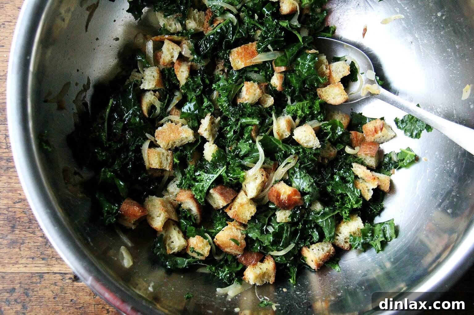 A large bowl generously filled with golden-brown toasted peasant bread cubes, vibrantly tossed with fresh kale and sweet caramelized onions.