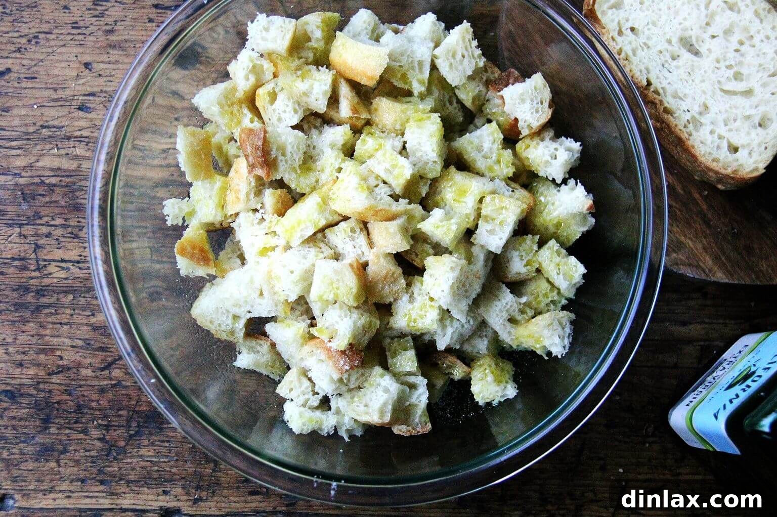 An overhead shot of a large glass bowl filled with cubed peasant bread generously tossed with olive oil and seasoned.