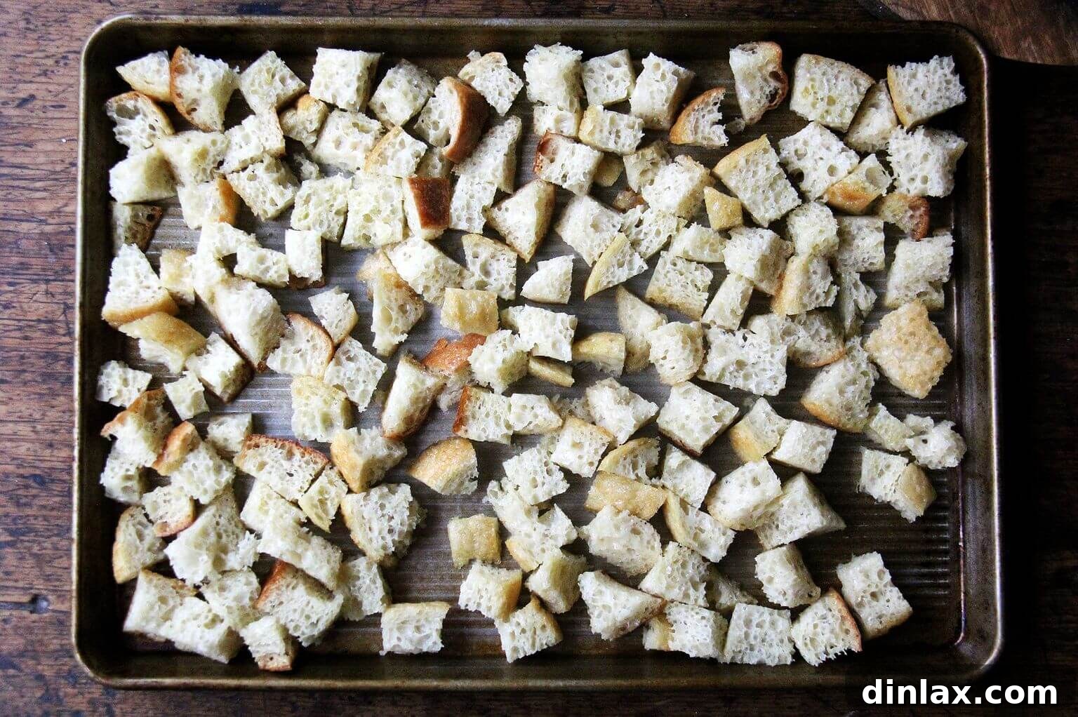 A sheet pan meticulously arranged with cubed peasant bread, thoroughly tossed in olive oil, ready for baking.