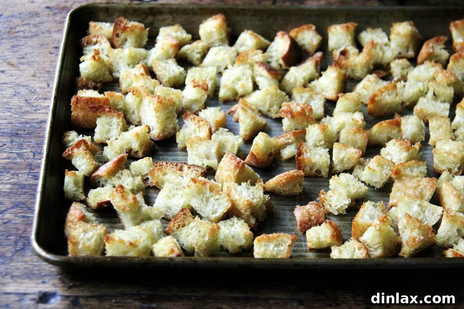 A sheet pan loaded with perfectly cubed and toasted peasant bread, golden brown and crisp from the oven.