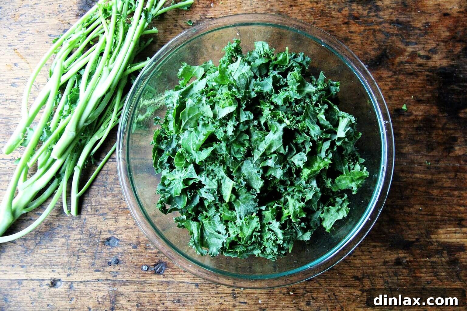 An overhead shot of a clear glass bowl generously filled with vibrant, freshly prepared kale leaves.
