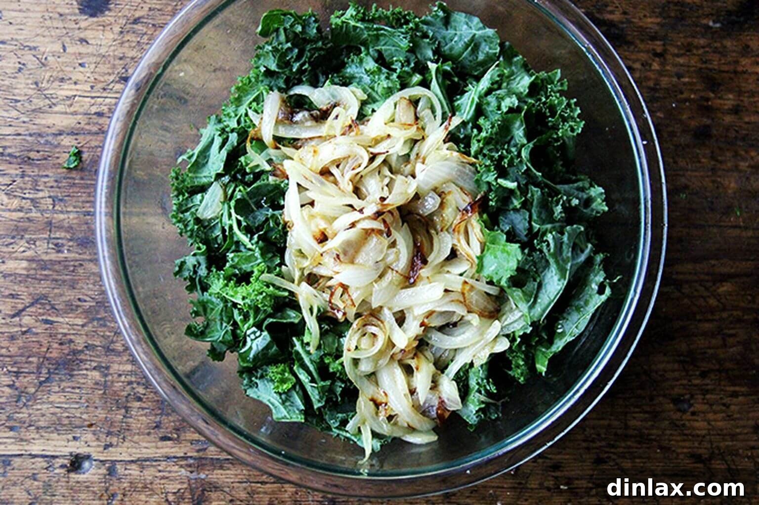 An overhead shot of a glass bowl filled with a harmonious blend of raw kale and deeply caramelized onions, gently tossed together.
