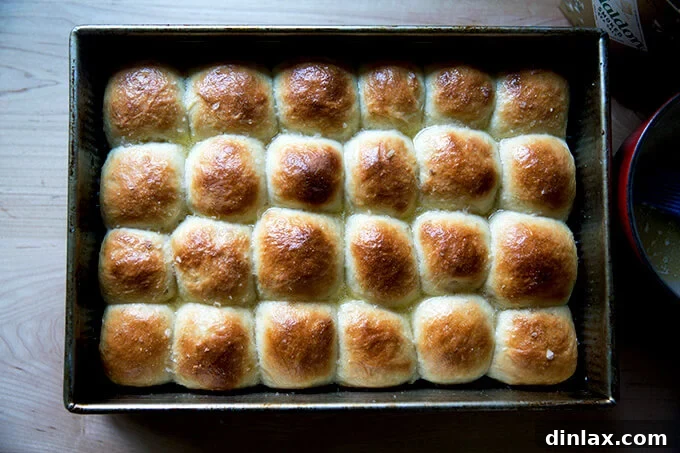 A close-up of freshly baked buttermilk pull-apart rolls being brushed with melted butter, adding a glistening finish.