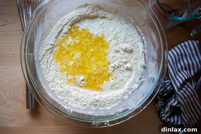 An overhead shot of a glass bowl after the wet ingredients, including the buttermilk mixture and melted butter, have been added to the dry ingredients for the buttermilk pull-apart rolls.