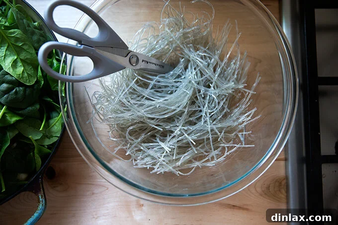 Japchae: Vegetarian Korean Glass Noodles 11 A large bowl filled with soaked and drained sweet potato noodles, scissors resting nearby, illustrating the step of cutting noodles to desired length.