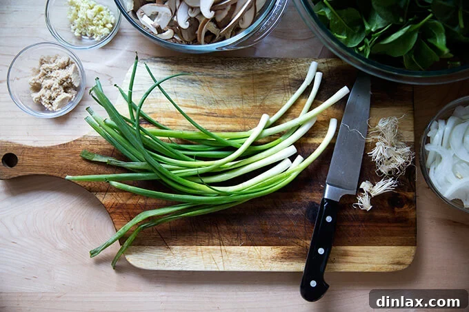 Japchae: Vegetarian Korean Glass Noodles 5 A cutting board laden with freshly sliced green scallions, diced garlic, and thinly sliced mushrooms, all prepped for cooking.