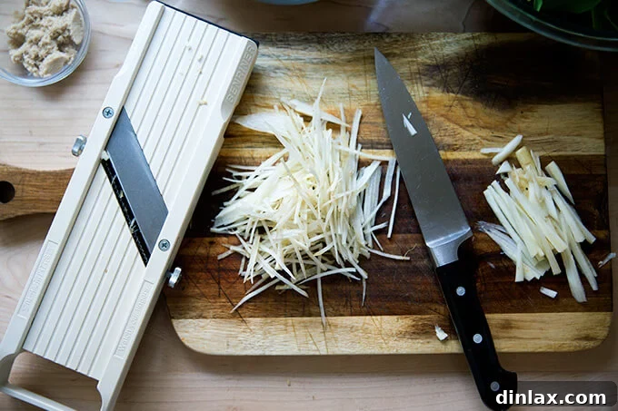 Japchae: Vegetarian Korean Glass Noodles 6 A collection of julienned carrots, showcasing both hand-cut and mandoline-sliced techniques for comparison on a cutting board.