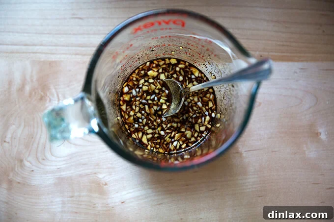 Japchae: Vegetarian Korean Glass Noodles 7 A measuring cup filled with the glossy, dark japchae sauce, featuring a spoon stirring its rich blend of soy sauce, garlic, and brown sugar.