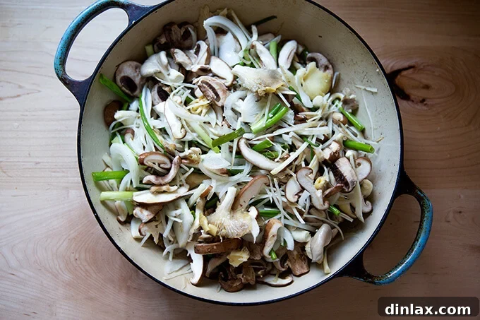 Japchae: Vegetarian Korean Glass Noodles 9 A close-up shot of chopped mushrooms, scallions, onions, and carrots coated with oil and water, nestled in a braiser, before the next layer is added.