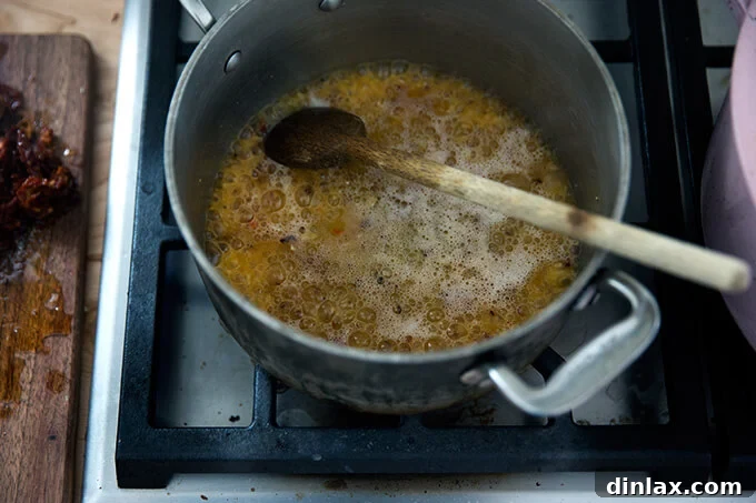 Vodka being poured into a saucepan, joining the sautéed butter, garlic, and red pepper flakes, about to simmer.