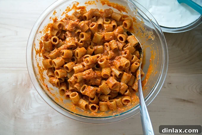 Cooked penne pasta, perfectly coated in a vibrant red vodka sauce, ready for layering in a baking dish.