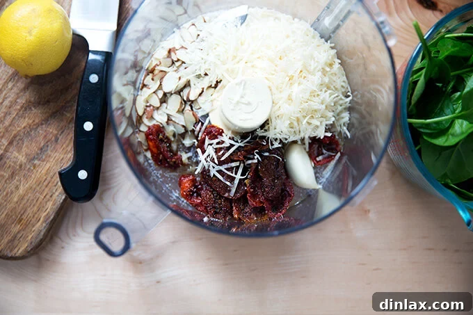 Sun-Kissed Tomato and Spinach Pesto Crostini 3 A food processor filled with almonds, sun-dried tomatoes, Parmesan, spinach, and garlic, ready to be blended into pesto.