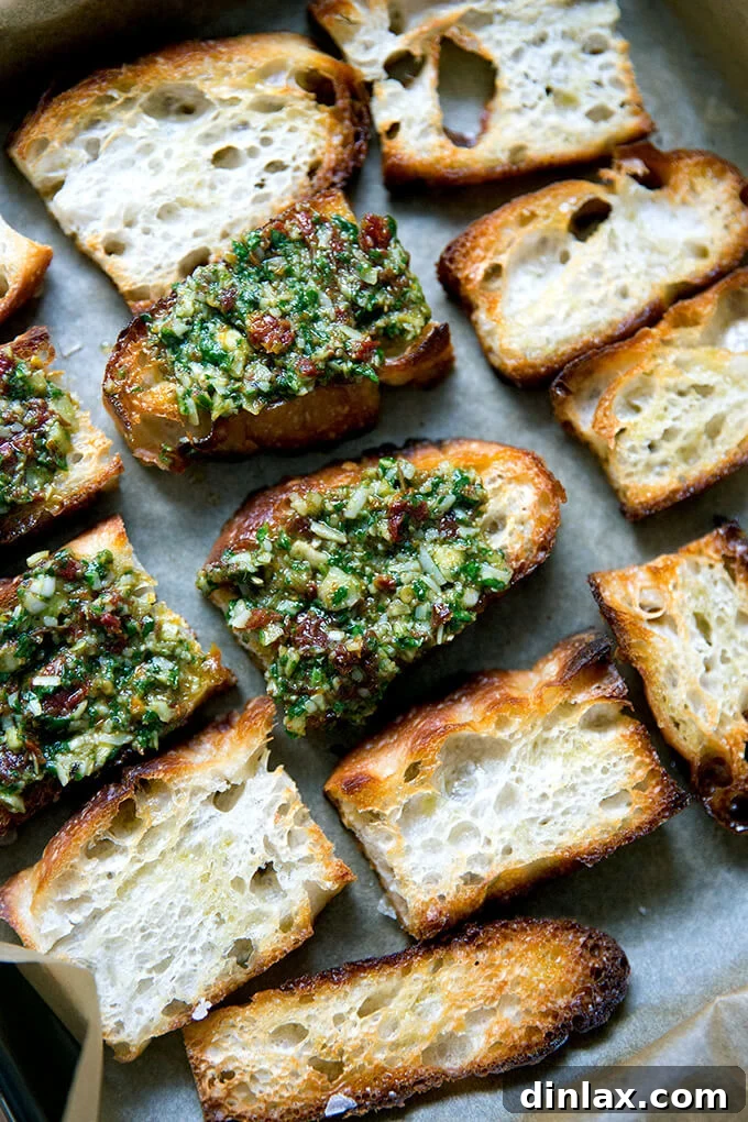 Sun-Kissed Tomato and Spinach Pesto Crostini 10 Crispy toast points artfully topped with a generous dollop of sun-dried tomato and spinach pesto, arranged on a baking sheet.