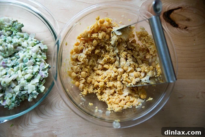 A bowl filled with chickpeas and pastry cutter to mash them up.