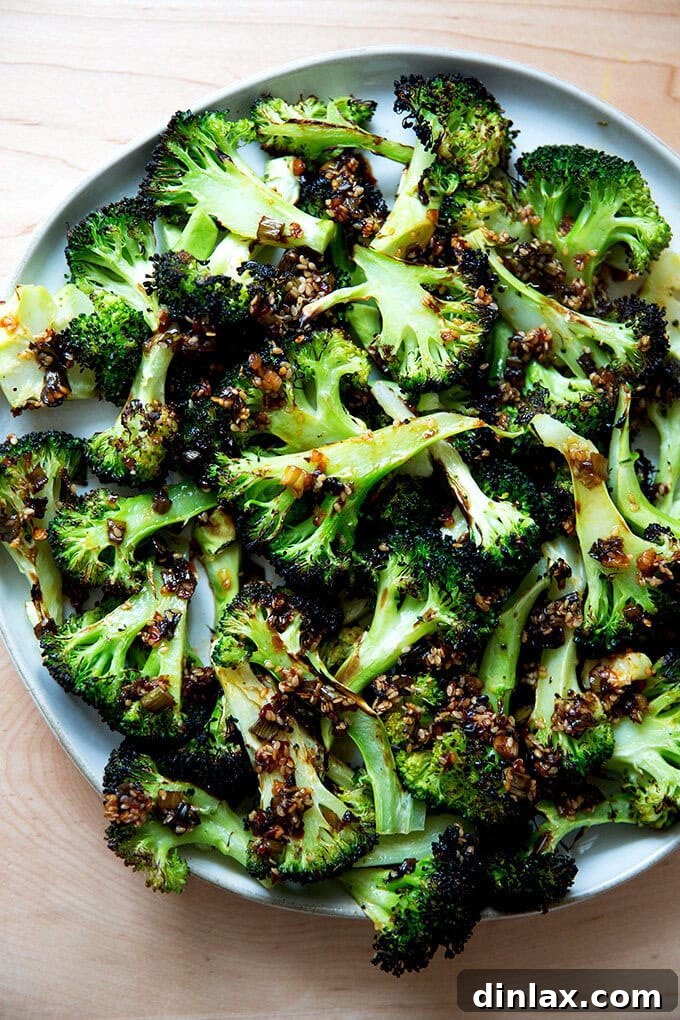 Crispy, charred broiled broccoli spears drizzled with a vibrant spicy sesame-scallion oil, served on a white plate, highlighting a quick and flavorful side dish.