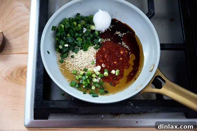 Ingredients for the spicy sesame-scallion oil laid out, including sesame oil, coconut oil, soy sauce, Sambal Oelek, sesame seeds, and sliced scallions, ready to be combined and heated.