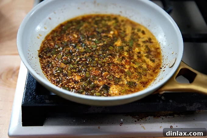 The spicy sesame-scallion oil simmering in a small skillet, with scallions and sesame seeds gently sizzling, indicating it's nearly ready to be poured over the broccoli.