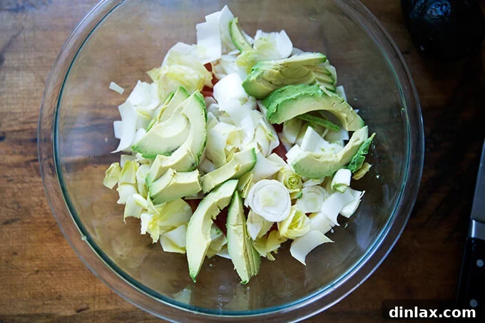 Citrus, crisp endive, and creamy avocado added to a bowl, ready for seasoning.