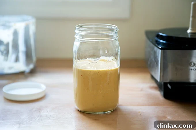 A glass jar filled with the freshly blended spicy cashew dressing, showing its creamy texture.