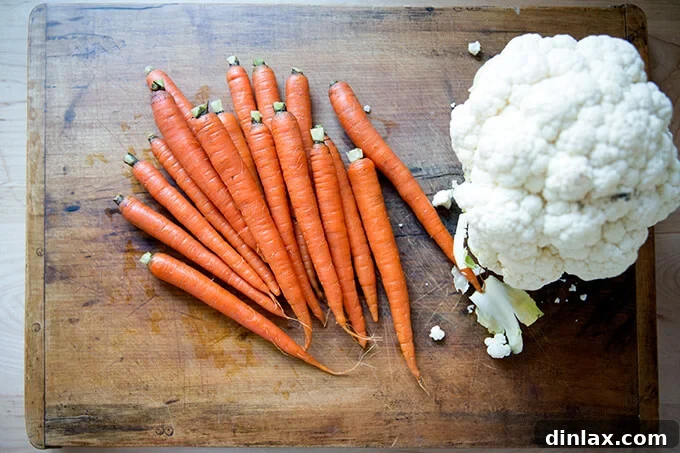A cutting board with whole carrots and a full head of cauliflower, ready for preparation.