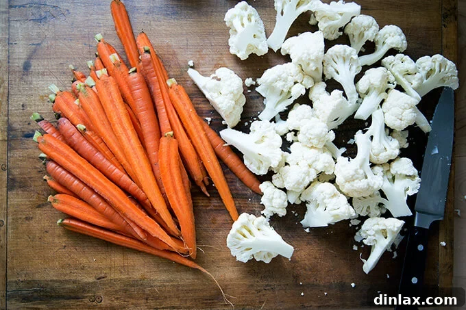 Halved carrots and neat cauliflower florets arranged on a cutting board, prepped for pickling.