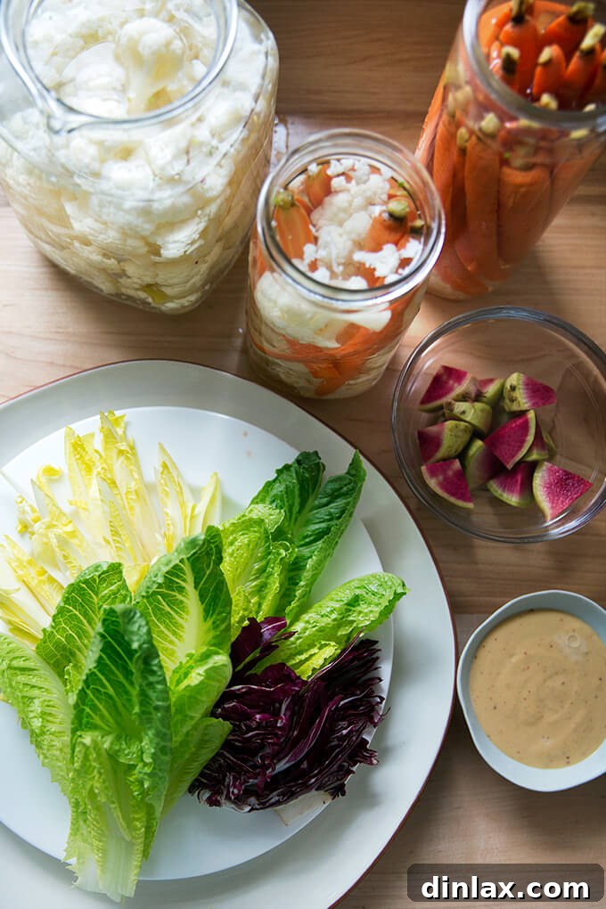 A beautifully arranged platter of pickled carrots and cauliflower alongside fresh endive, radicchio, and radishes, served with a creamy dip.
