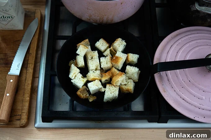 Golden Cheddar Broccoli Bisque 13 Cubed focaccia bread is toasting in olive oil in a skillet, transforming into golden, crispy croutons.