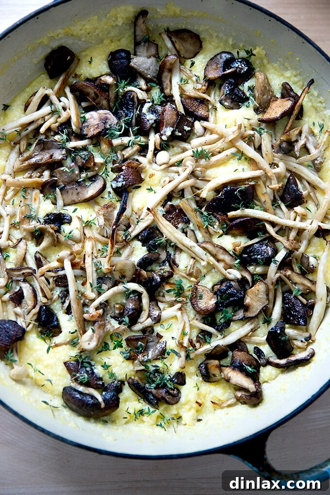 A skillet of creamy polenta artfully topped with a generous layer of glistening roasted mushrooms and fresh thyme.