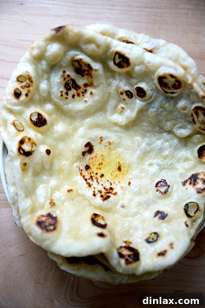A bowl of freshly baked naan, brushed with butter and stacked, ready to be served.