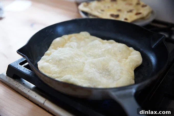 A round of naan cooking in a hot cast-iron skillet, beginning to puff.