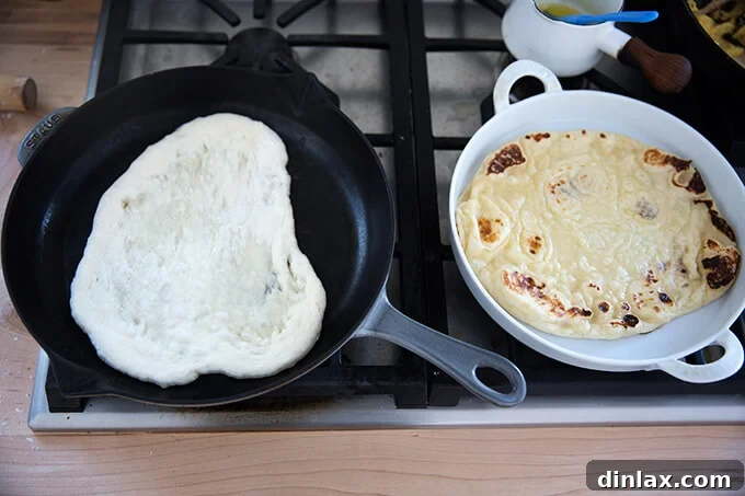 Freshly cooked naan being brushed with melted butter straight out of the skillet.