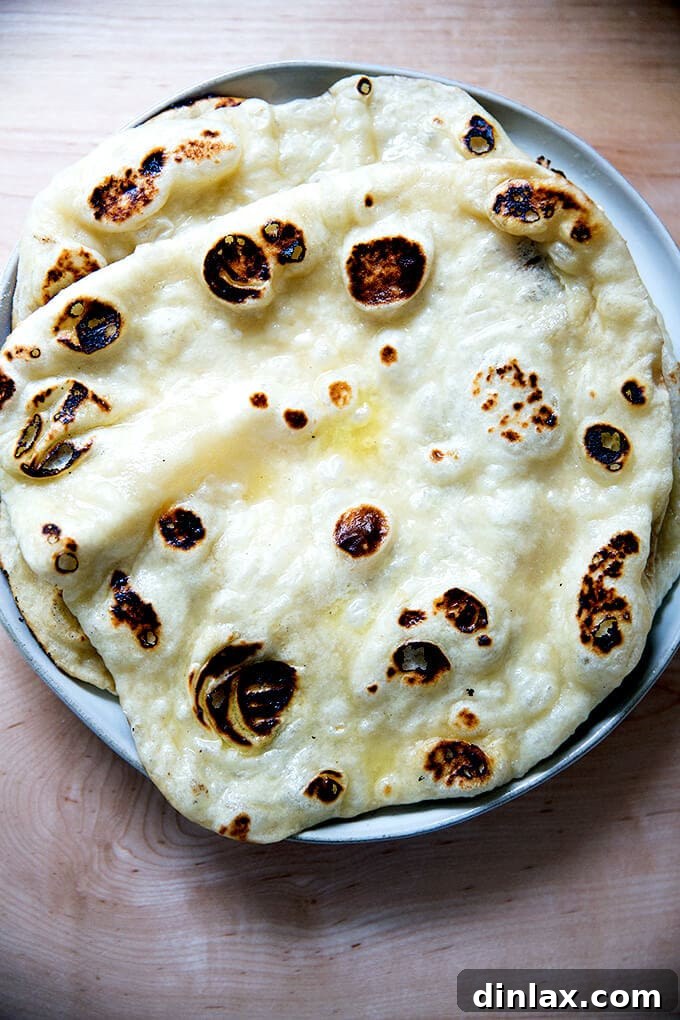 A stack of warm, freshly baked naan resting on a plate, covered with a tea towel.