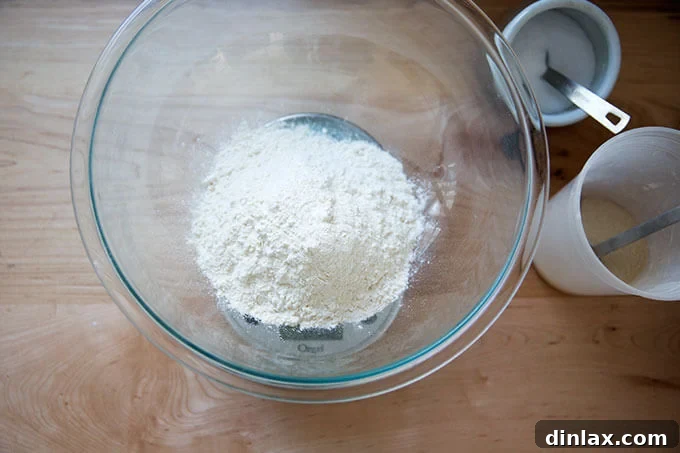 A bowl of all-purpose flour with piles of instant yeast and kosher salt on a wooden surface.