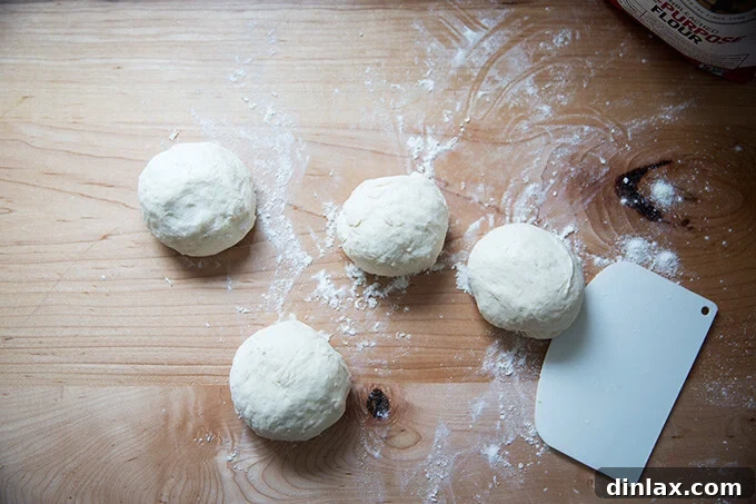 Four smooth balls of naan dough arranged on a floured work surface.