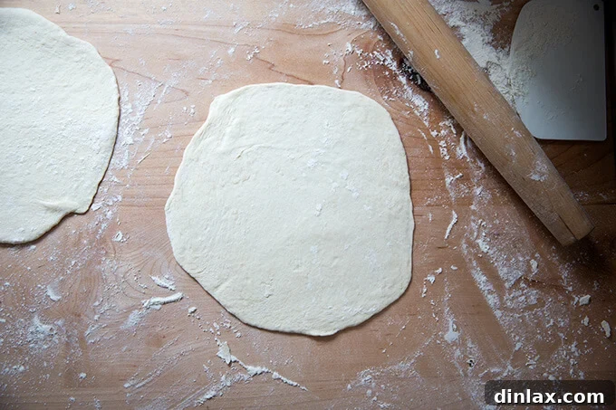 Two rounds of naan dough rolled out thinly on a floured work surface, ready for cooking.