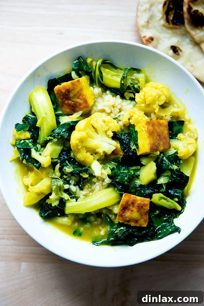 A vibrant bowl of vegetarian and tofu curry, rich with cauliflower and kale, served alongside fluffy rice.