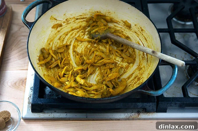 Onions coated in a rich mixture of curry spices, sizzling gently in a stovetop skillet.