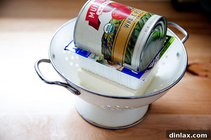 Tofu being pressed in a colander with a heavy container on top.