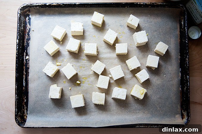 Cubed and seasoned tofu spread on a parchment-lined baking sheet, ready for the oven.