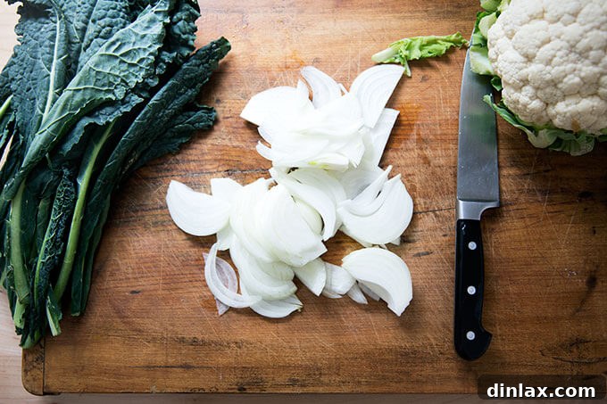 Sliced kale, onions, and cauliflower florets on a wooden cutting board, prepped for curry.