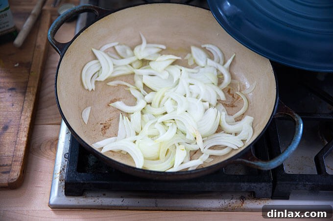 Thinly sliced onions gently sautéing in olive oil in a skillet on the stovetop.