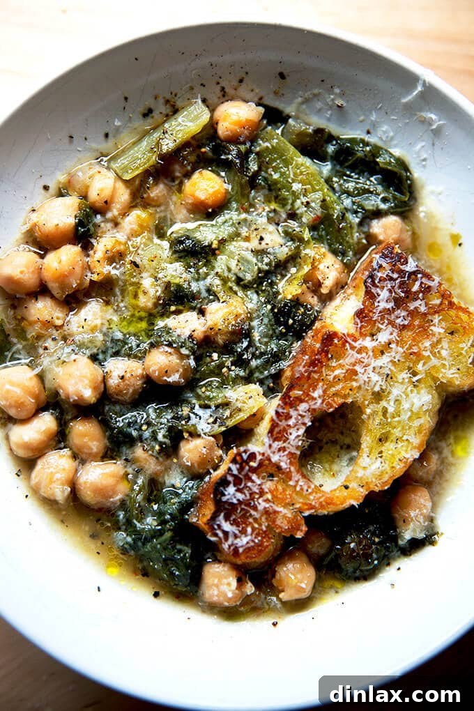 A beautifully presented bowl of chickpea and escarole soup, garnished with freshly shaved Parmesan and toasted bread.