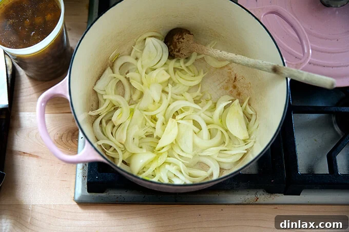 Sliced onions beginning to soften in olive oil within a Dutch oven on the stovetop.