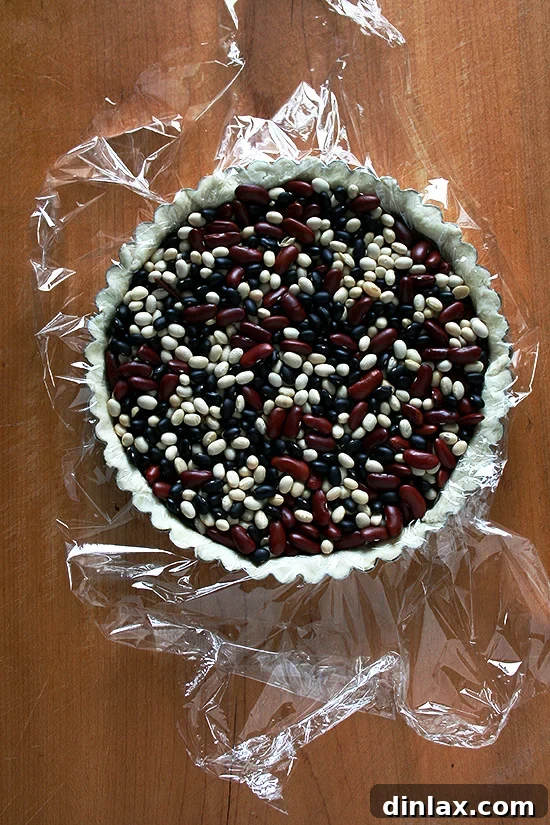 Tart shell prepared for blind baking, lined with plastic wrap and dried beans.