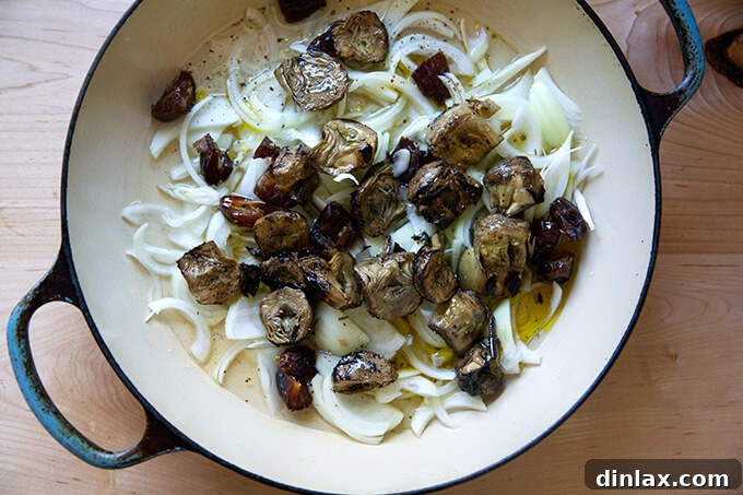 A skillet filled with a flavorful mixture of sliced onions, drained artichoke hearts, and chopped dates, tossed with olive oil, white wine, and water, seasoned with salt and pepper.
